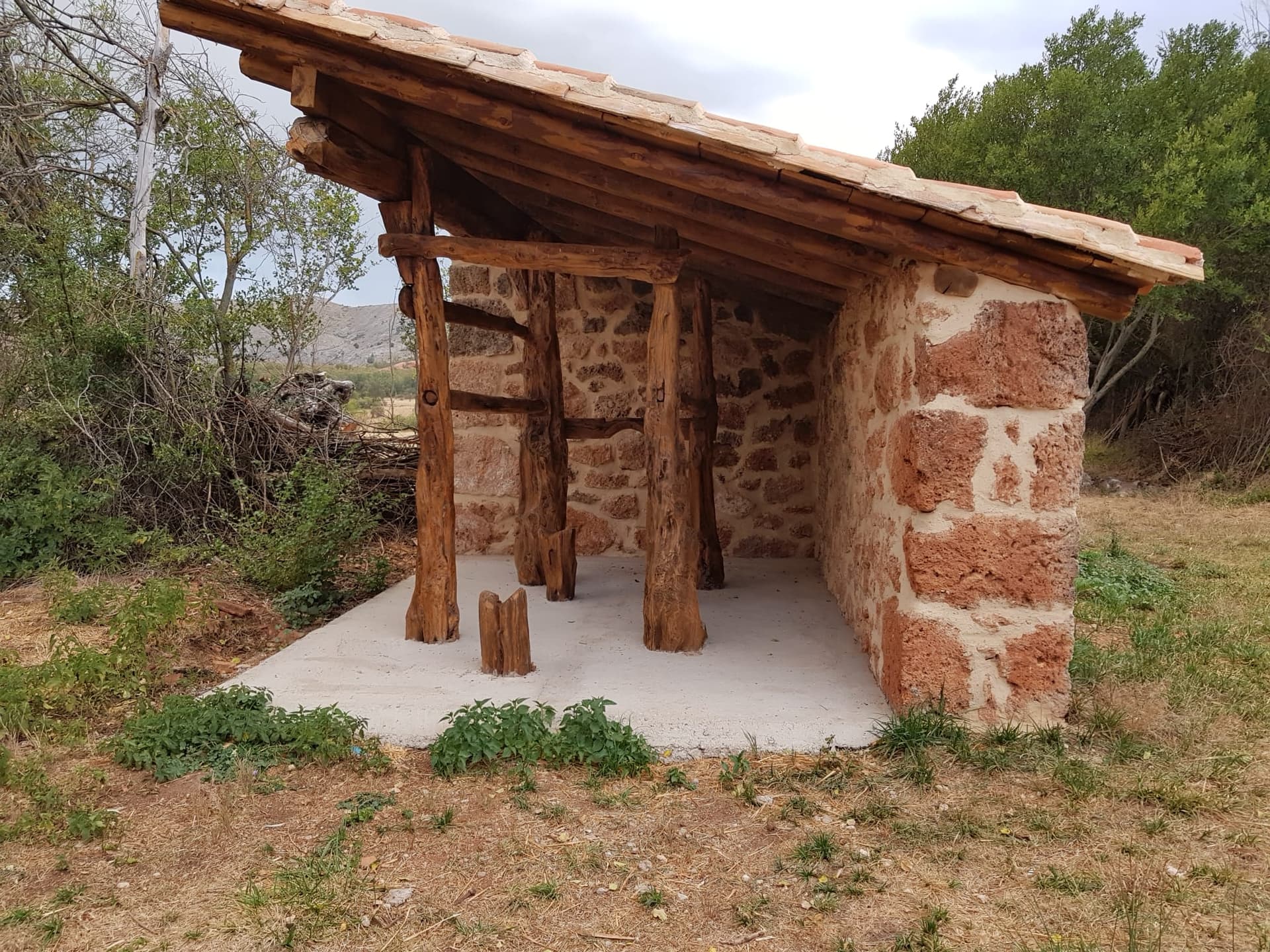 Potro de herrar restaurado: estructura de madera y piedra arenisca rojiza con tejadillo de teja árabe