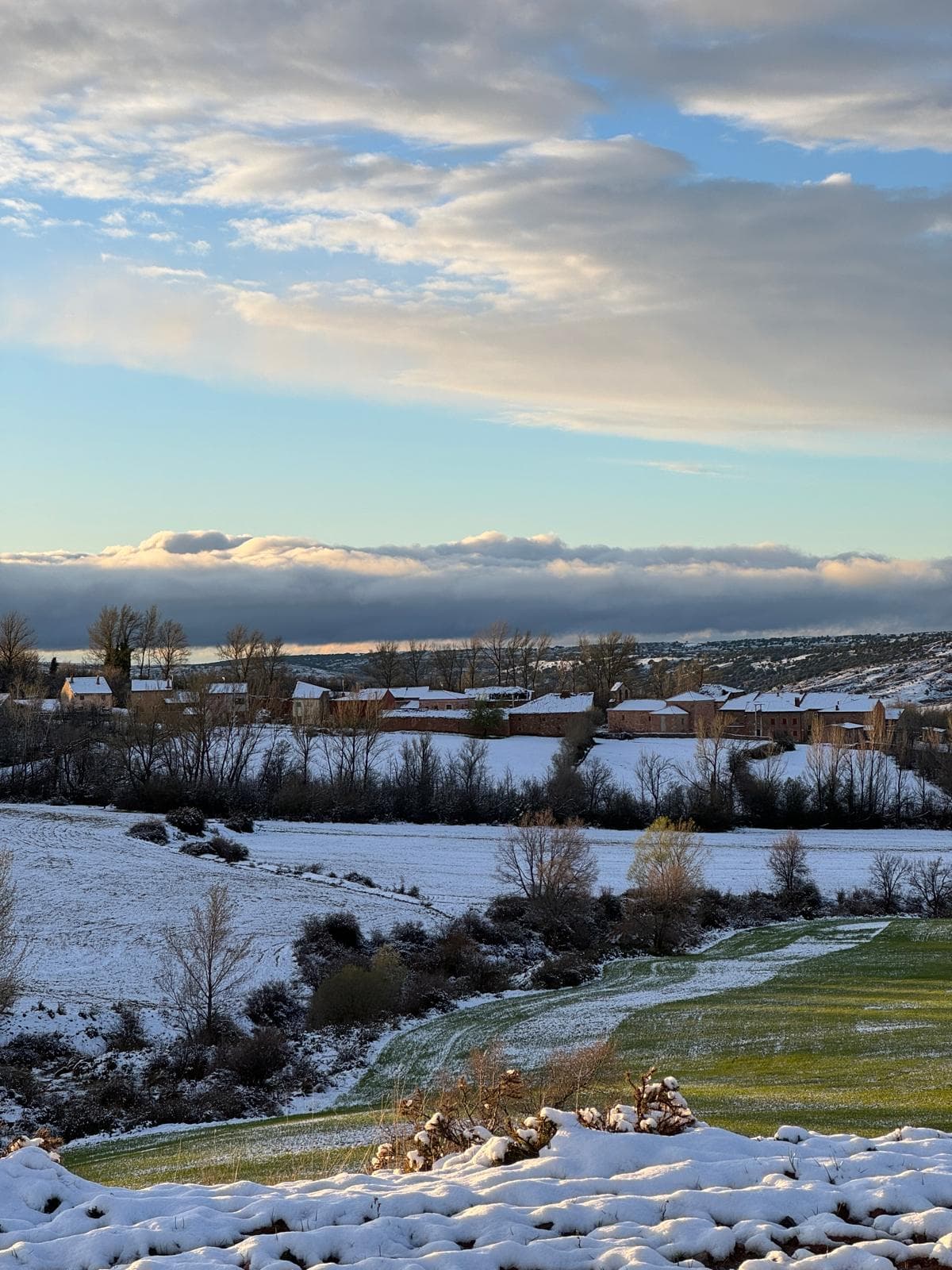 Rebollosa de Pedro cubierto de nieve al atardecer, con un banco de nubes bajas iluminado por la luz cálida del ocaso
